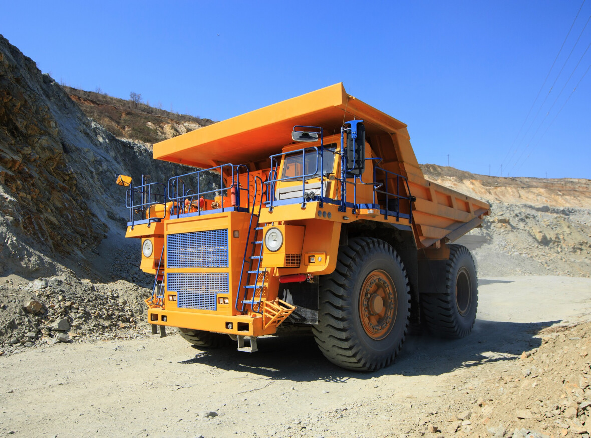 Large yellow mining dump truck on the road on a sunny day. Large-sized equipment for the transportation of rock mass in an ore quarry. Large yellow mining dump truck on the road on a sunny day. Large-sized equipment for the transportation of rock mass in an ore quarry.