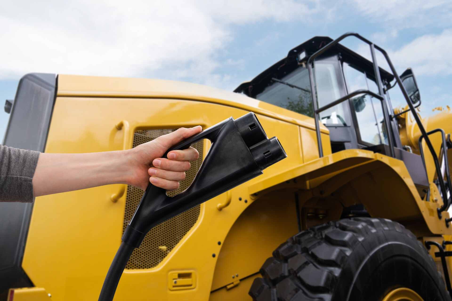 Hand with electric plug on a background of electric tractor