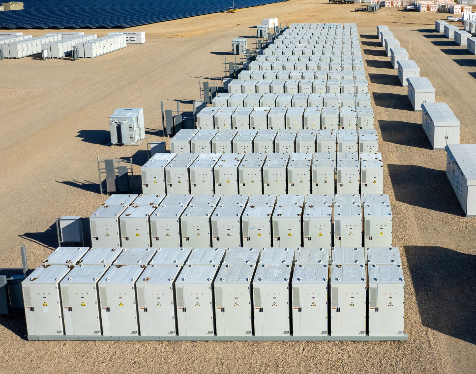 utility scale battery energy storage Aerial view of industrial battery units storing electricity in the desert. In the distance are solar panels and mountains.
